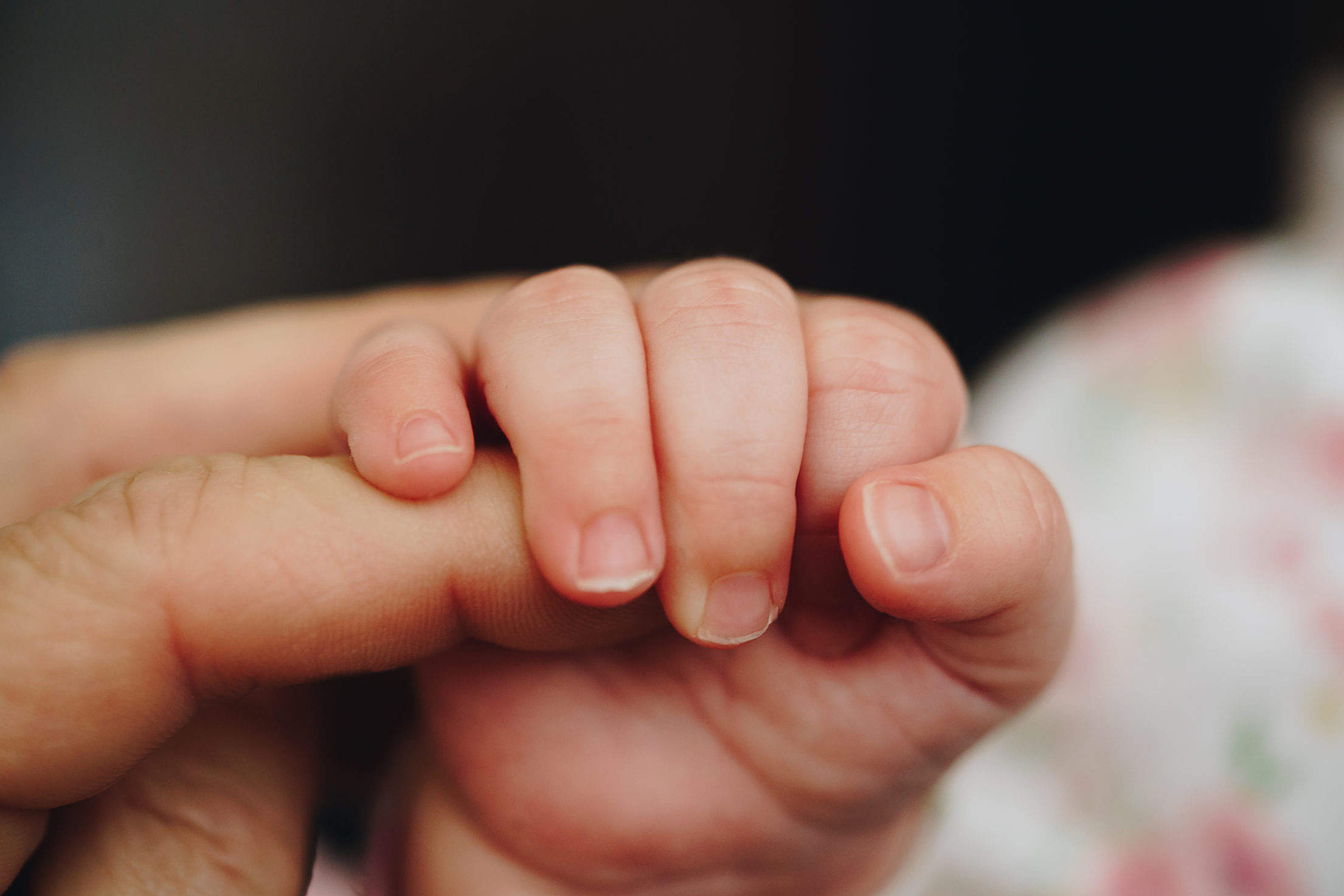 A baby holding an adult's finger.